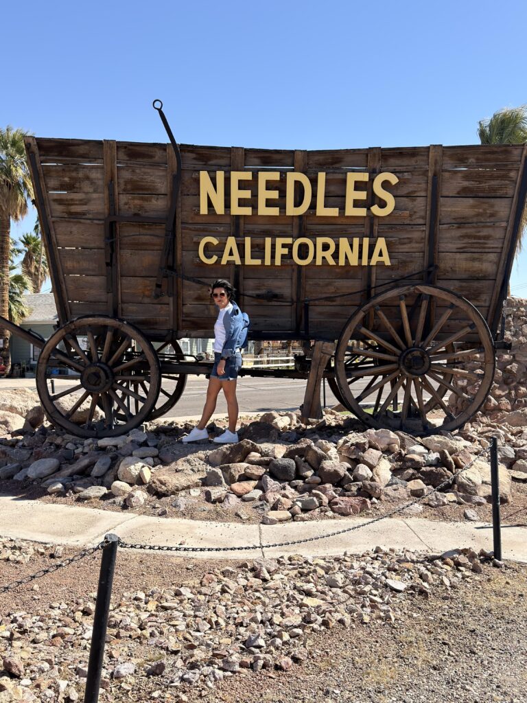 Frau vor dem großen Holzplanwagen Wahrzeichen mit Needles California Schriftzug