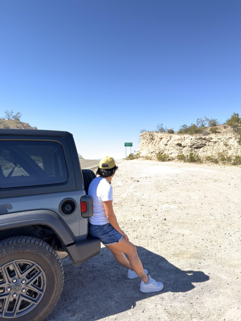 Frau lehnt am grauen Jeep Wrangler am Sitgreaves Pass mit Route-66-Schild im Hintergrund