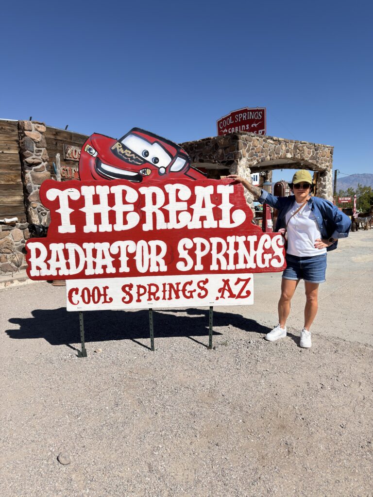 Frau vor The Real Radiator Springs Schild mit Lightning McQueen in Cool Springs Arizona