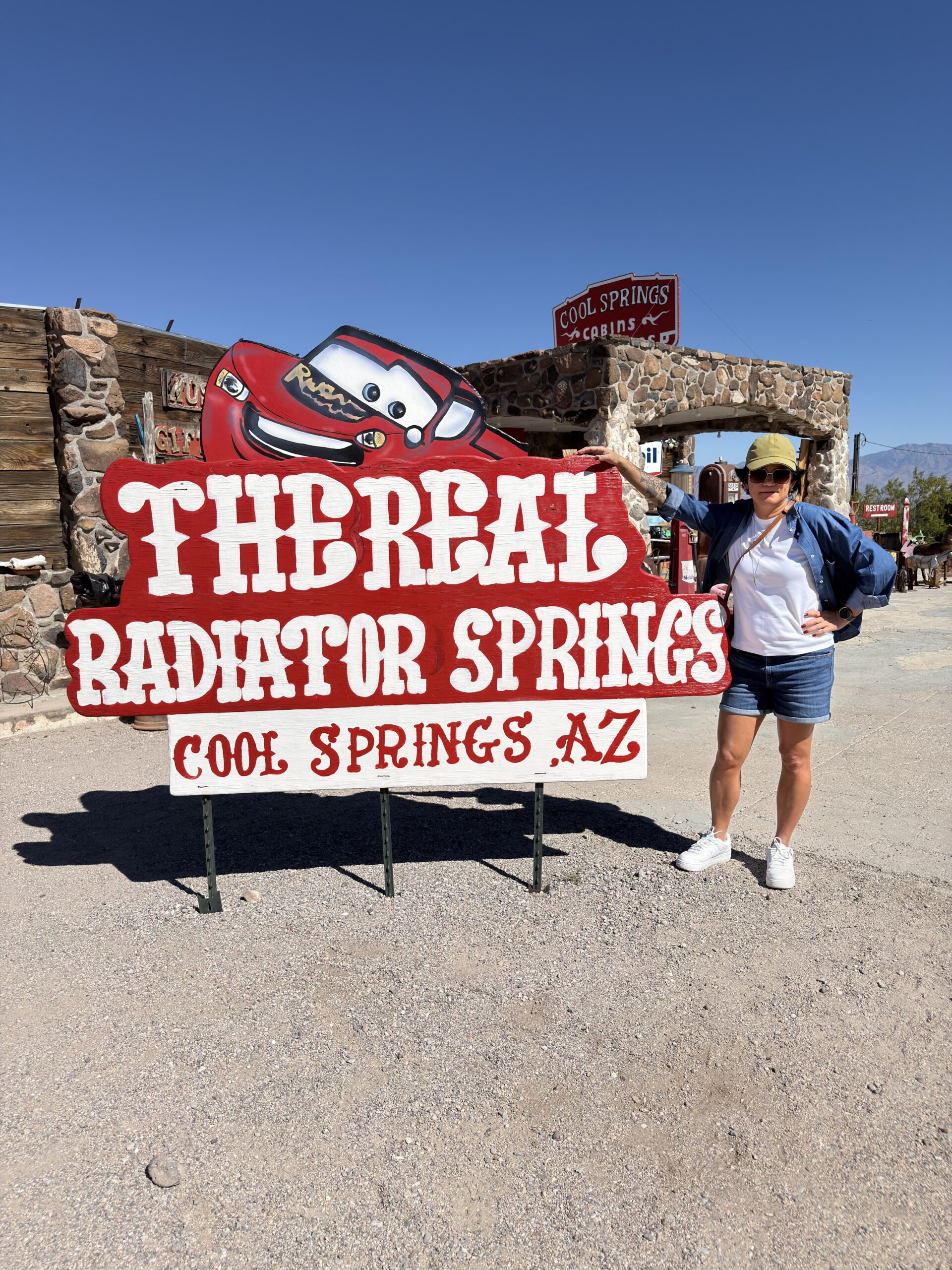 Frau vor The Real Radiator Springs Schild mit Lightning McQueen in Cool Springs Arizona