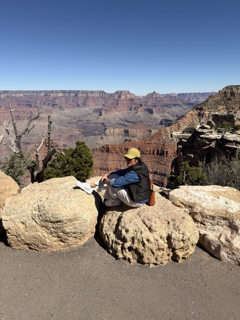 Frau sitzt auf Felsen am Grand Canyon South Rim mit weitem Blick in den Canyon
