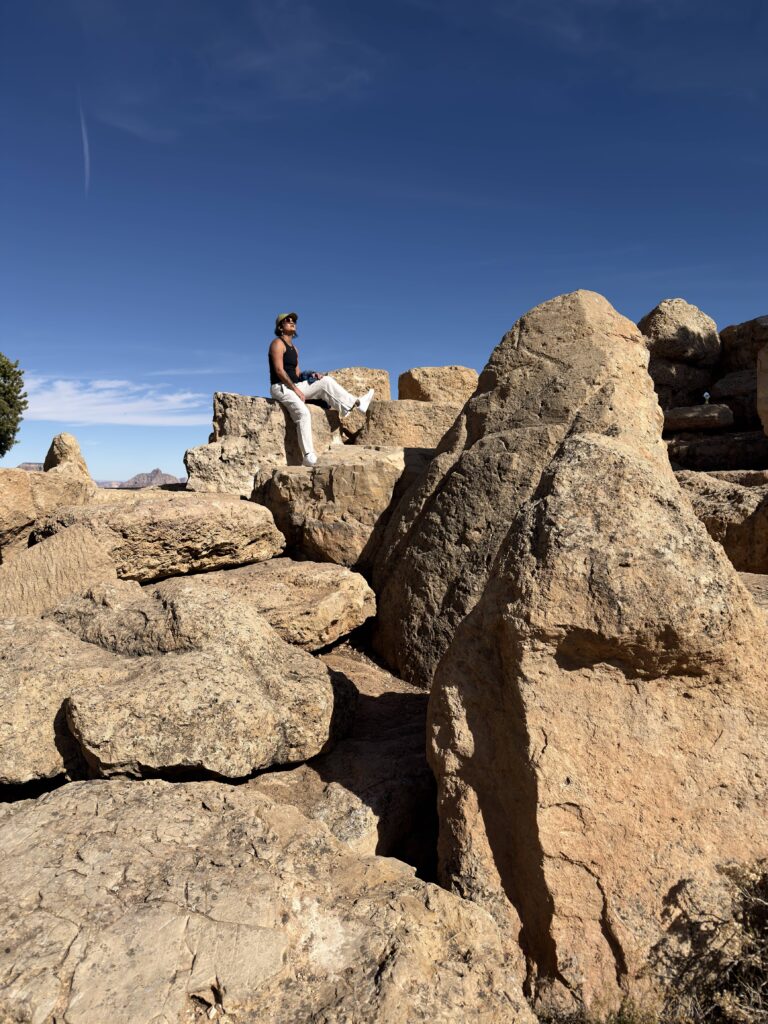 Frau sitzt hoch auf Felsen am Grand Canyon South Rim unter blauem Himmel