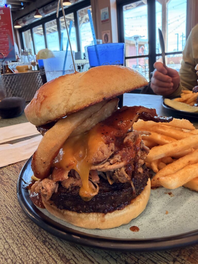 Draufsicht auf zwei Big Tex Burger mit Pommes frites auf rustikalem Tisch von oben, dazu ein Glas Cola.