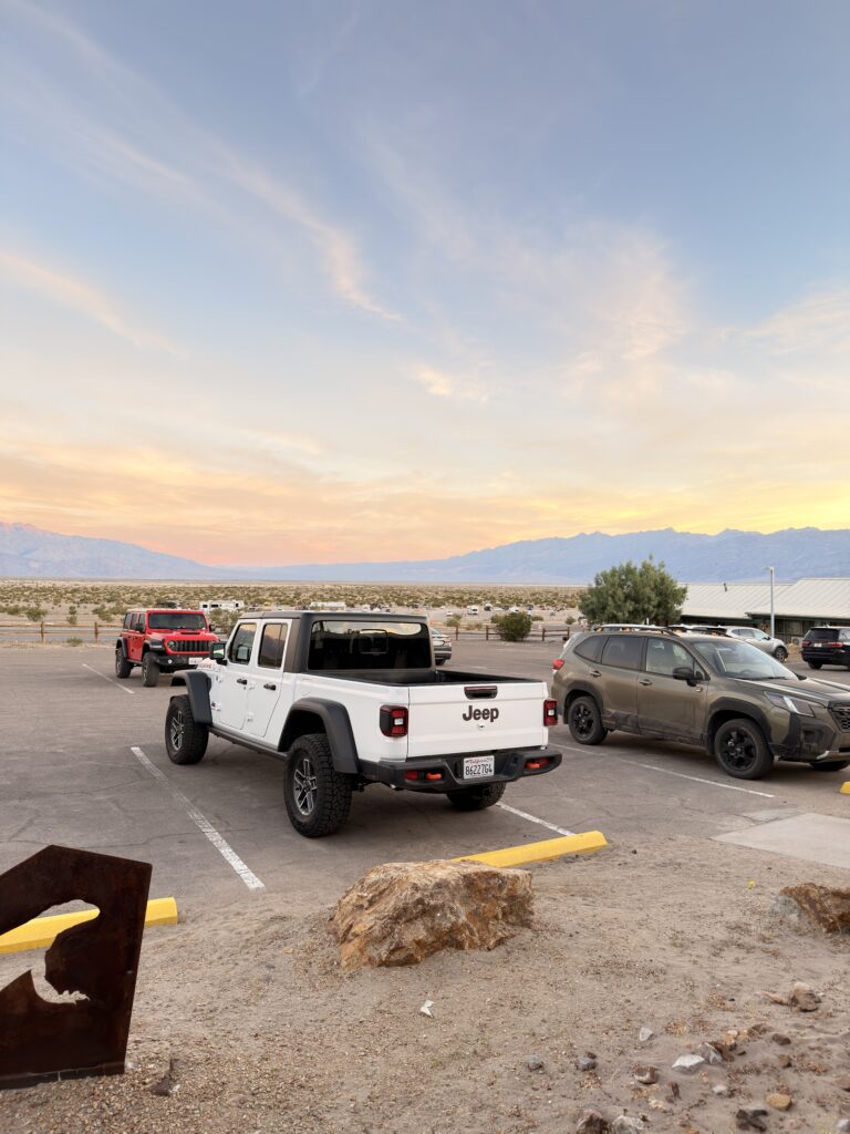 Weißer Jeep Gladiator auf einem Parkplatz im Death Valley bei Sonnenuntergang, im Hintergrund die weite Wüstenebene und das Bergpanorama in warmem Abendlicht
