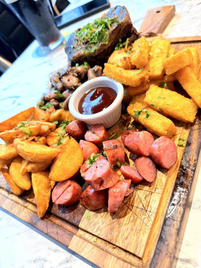 Mixed Grill Board bei The Ribs Gaucho BBQ Dublin mit Steak, Würstchen, Pommes und BBQ-Sauce auf Holzbrett