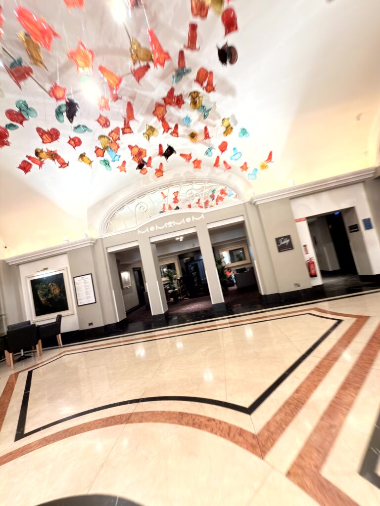 Prachtvoller Eingangsbereich des Riu Plaza The Gresham Dublin mit bunter Glaskunstinstallation an der Decke und Marmorböden