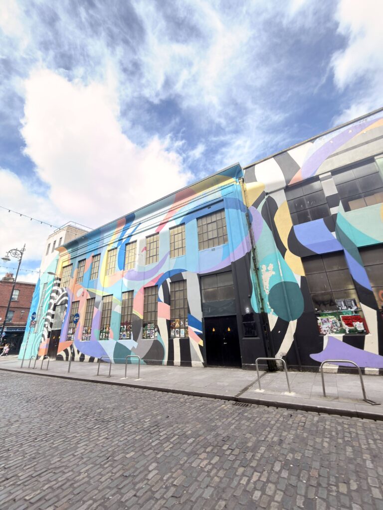 Buntes großformatiges Street-Art-Wandbild auf einer Gebäudefassade im Temple Bar Viertel Dublin mit Kopfsteinpflaster im Vordergrund