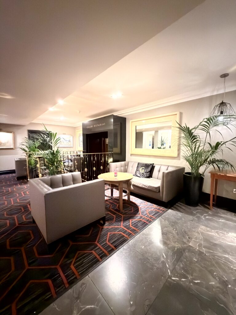Elegante Hotelbar Lounge mit grauen Sofas, Palmen und gemustertem Teppich im Riu Plaza The Gresham Dublin