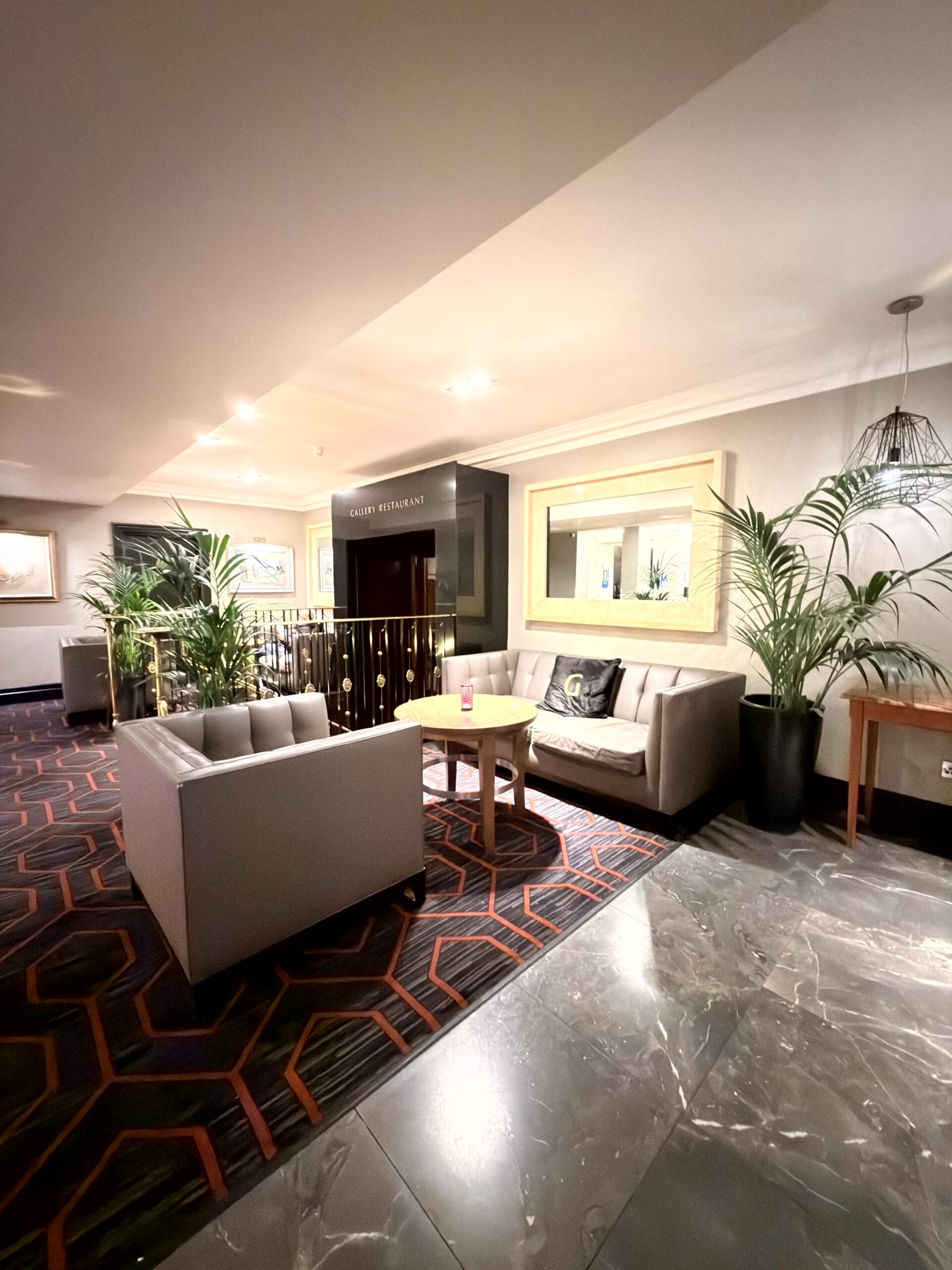 Elegante Hotelbar Lounge mit grauen Sofas, Palmen und gemustertem Teppich im Riu Plaza The Gresham Dublin