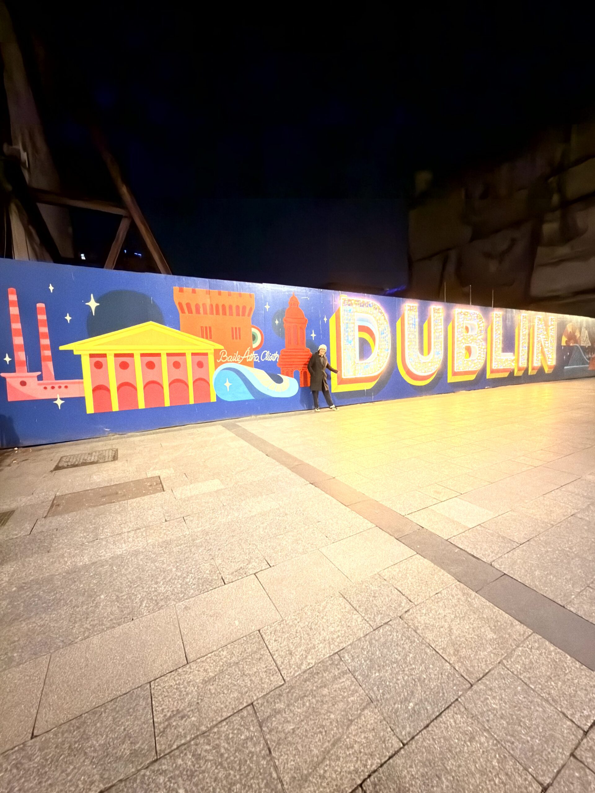 Buntes Dublin-Wandbild mit Stadtmotiven und Schriftzug DUBLIN bei Nacht, Person davor