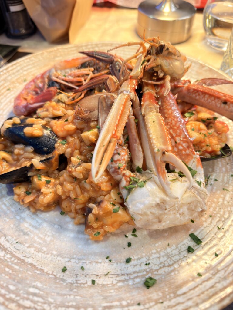 Großer Teller mit Risotto ai Frutti di Mare, belegt mit Scampi, Krebsscheren, Muscheln und frischer Petersilie, serviert im Restaurant El Refol in Garda am Gardasee