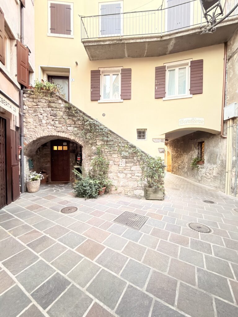 Schmale Kopfsteinpflastergasse in der Altstadt von Garda mit bunten Häuserfassaden und Blumenschmuck