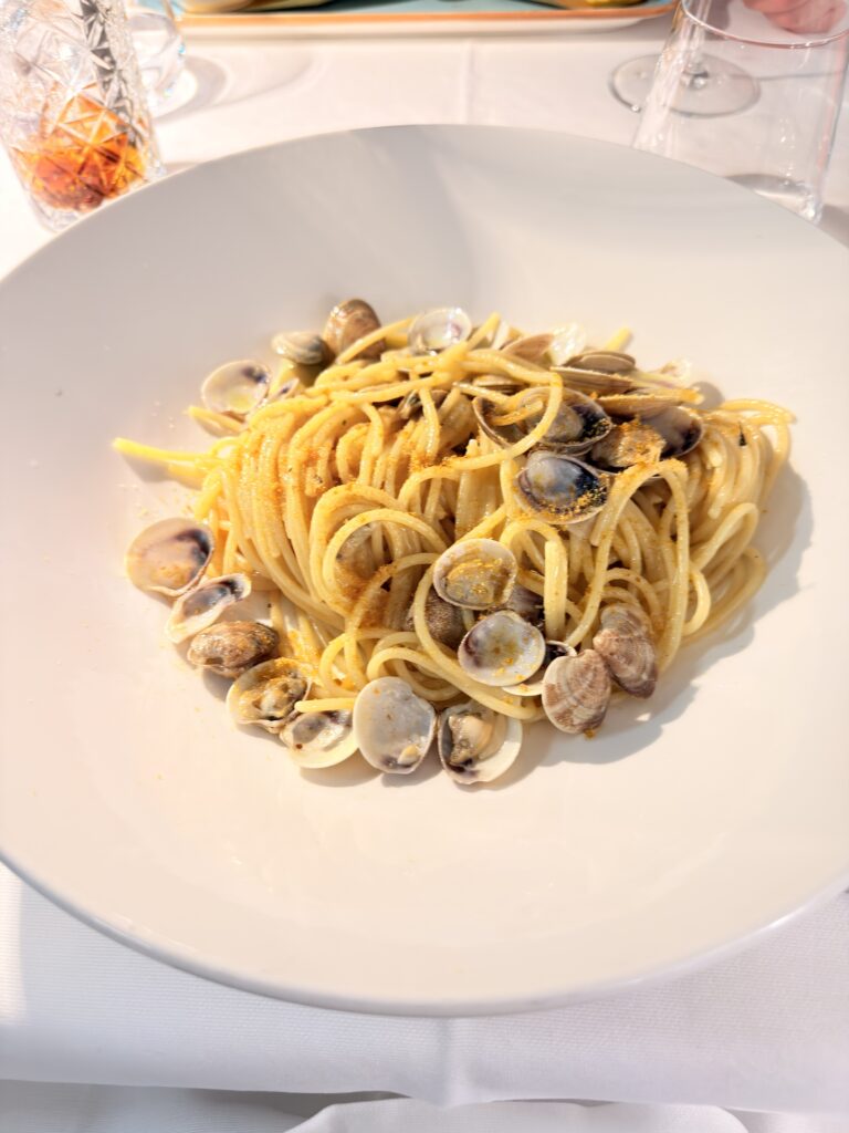 Spaghetti alle Vongole mit frischen Venusmuscheln und goldgelbem Bottarga-Abrieb auf weißem Tiefteller, serviert im Hotel Ristorante Giardinetto