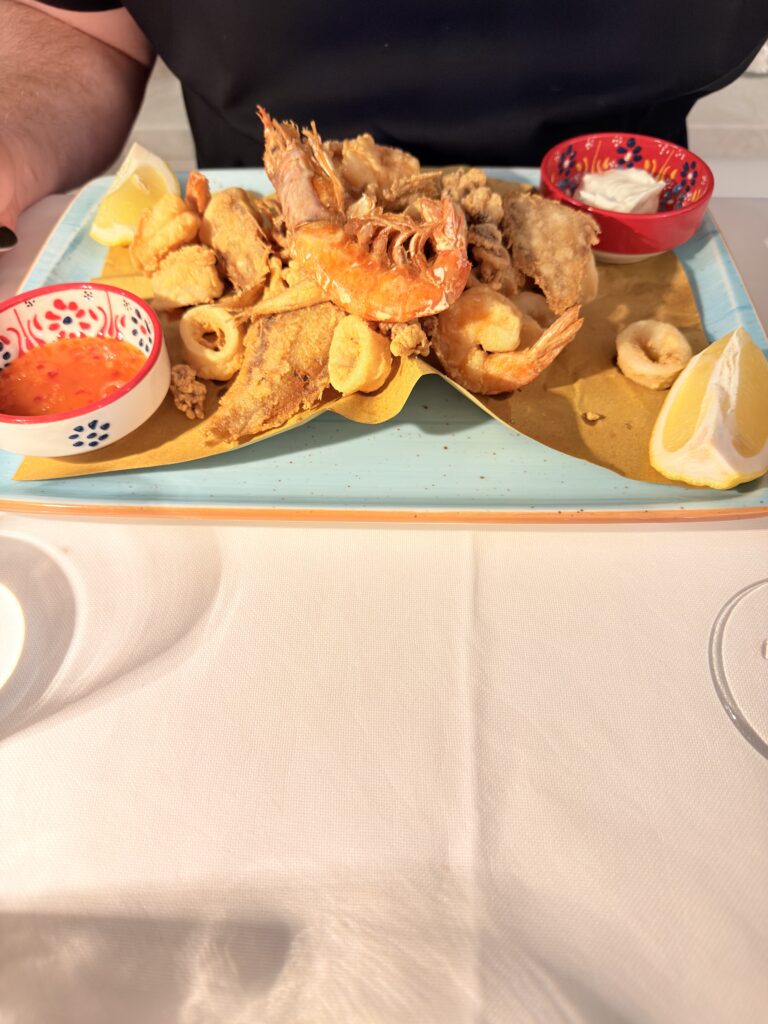 Fritto Misto di Mare auf hellblauem Teller mit knusprig frittiertem Scampi, Calamari, Garnelen und Fisch, serviert mit Zitronenspalten sowie Dips aus Tomatensauce und Aioli im Hotel Ristorante Giardinetto
