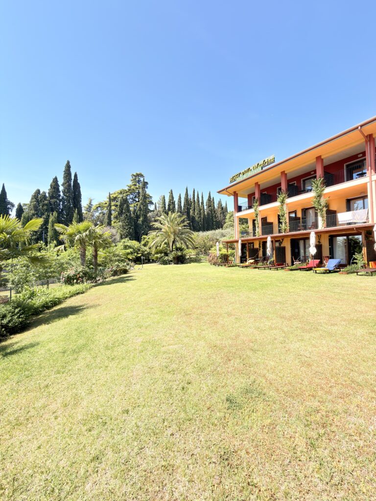 Gepflegter Hotelgarten mit Palmen und Zypressen vor dem Hotel Villa Mandrina in Garda am Gardasee
