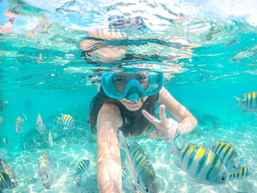 Unterwasser-Selfie einer Frau mit Taucherbrille, umgeben von einem Schwarm gestreifter Fische in Maragogi
