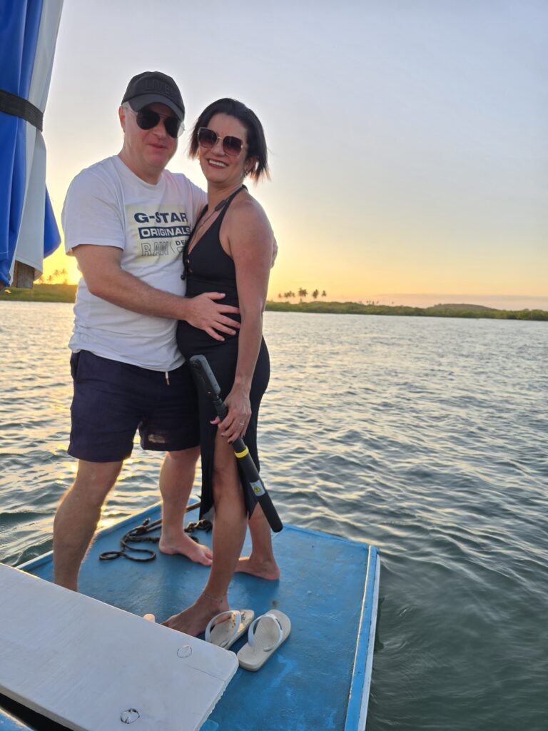 Paar auf dem Bug eines blauen Bootes beim Sonnenuntergang am Pontal de Maracaípe