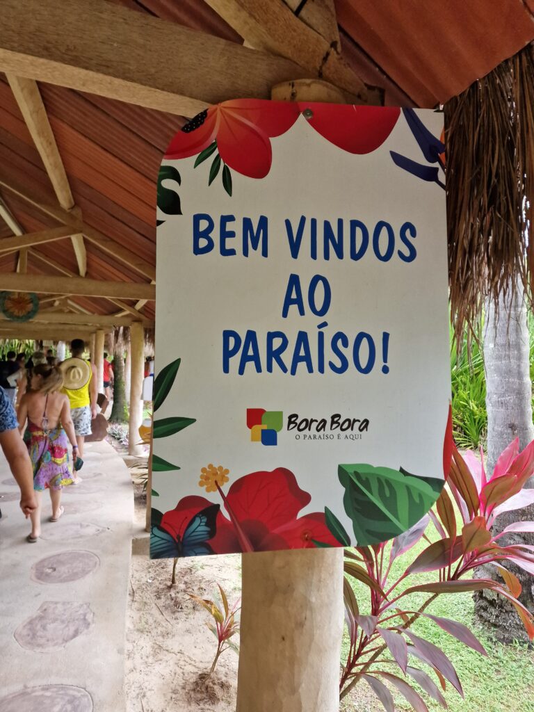 Bunt bemaltes Schild "Bem Vindos ao Paraíso" mit Bora-Bora-Logo am Eingang eines Strandclubs bei Carneiros