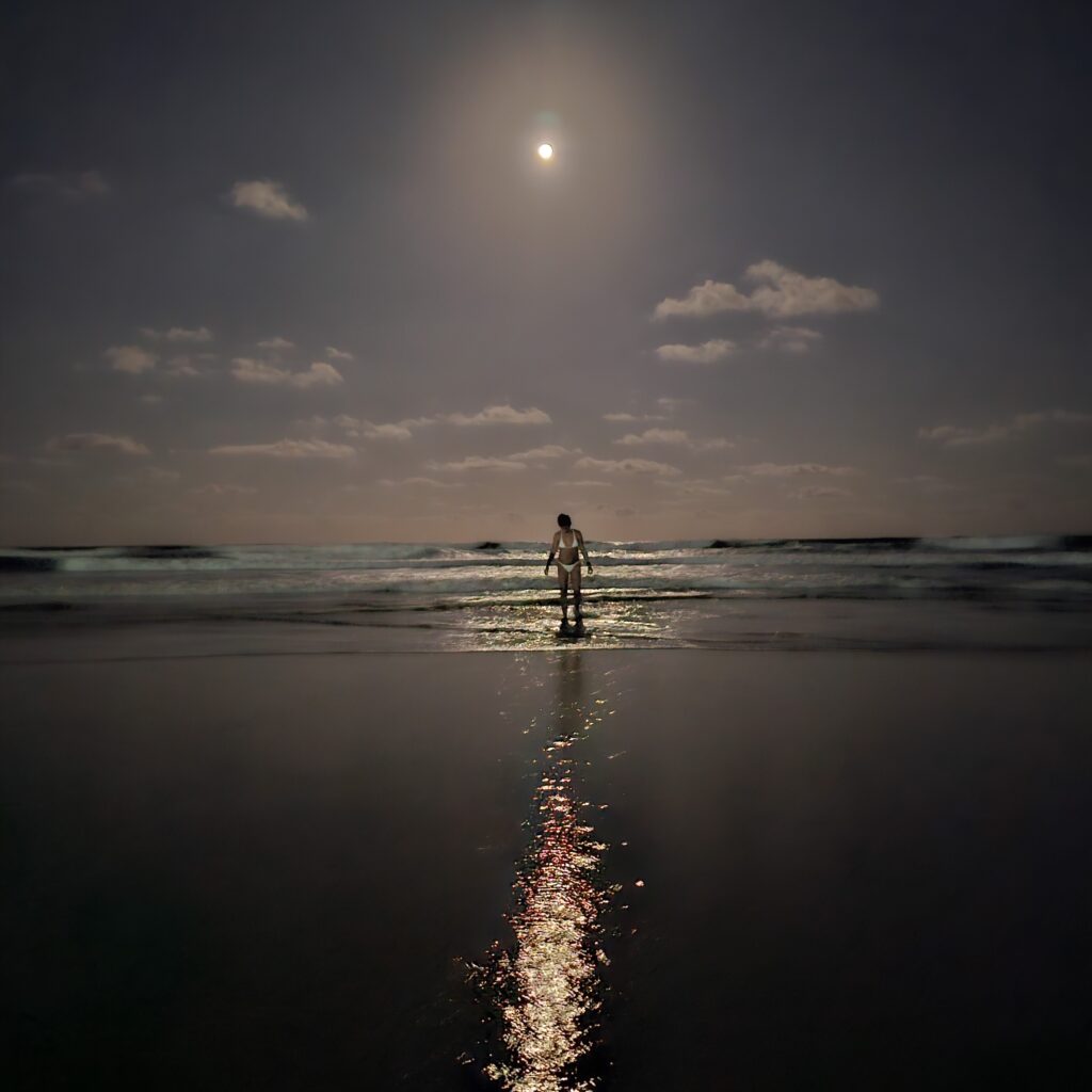 Person watet nachts ins Meer am Praia do Cupe, der Vollmond spiegelt sich als leuchtender Streifen auf dem Wasser