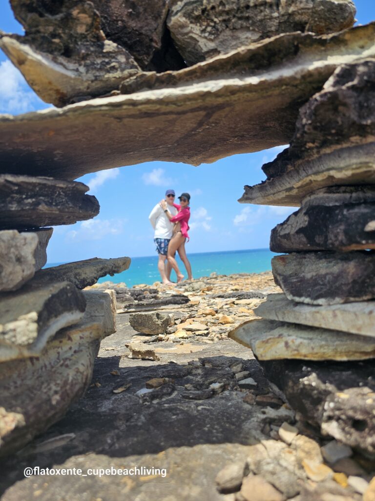 Paar steht am Meer, fotografiert durch eine natürliche Felsspalte im Vordergrund bei der Ilha de Santo Aleixo