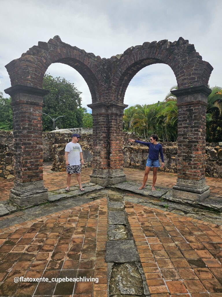 Paar steht zwischen zwei alten Ziegelbögen der Ruinas Convento Carmelita, umgeben von Palmen