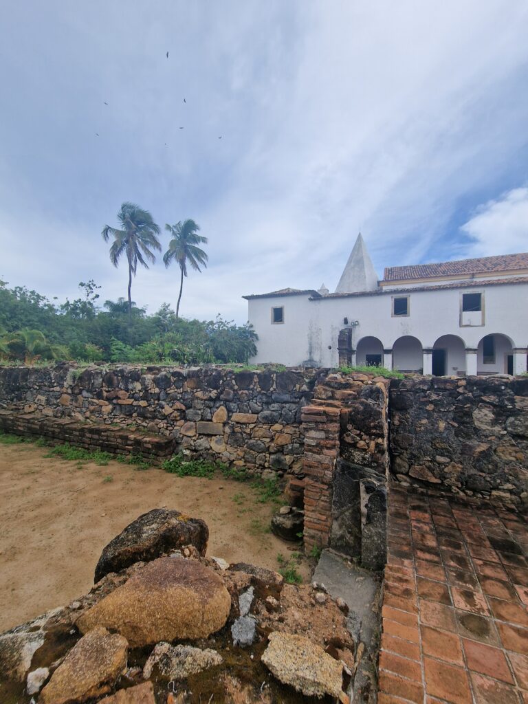 Weißes Kirchengebäude der Igreja de Nazaré mit alten Steinmauern und Palmen im Vordergrund