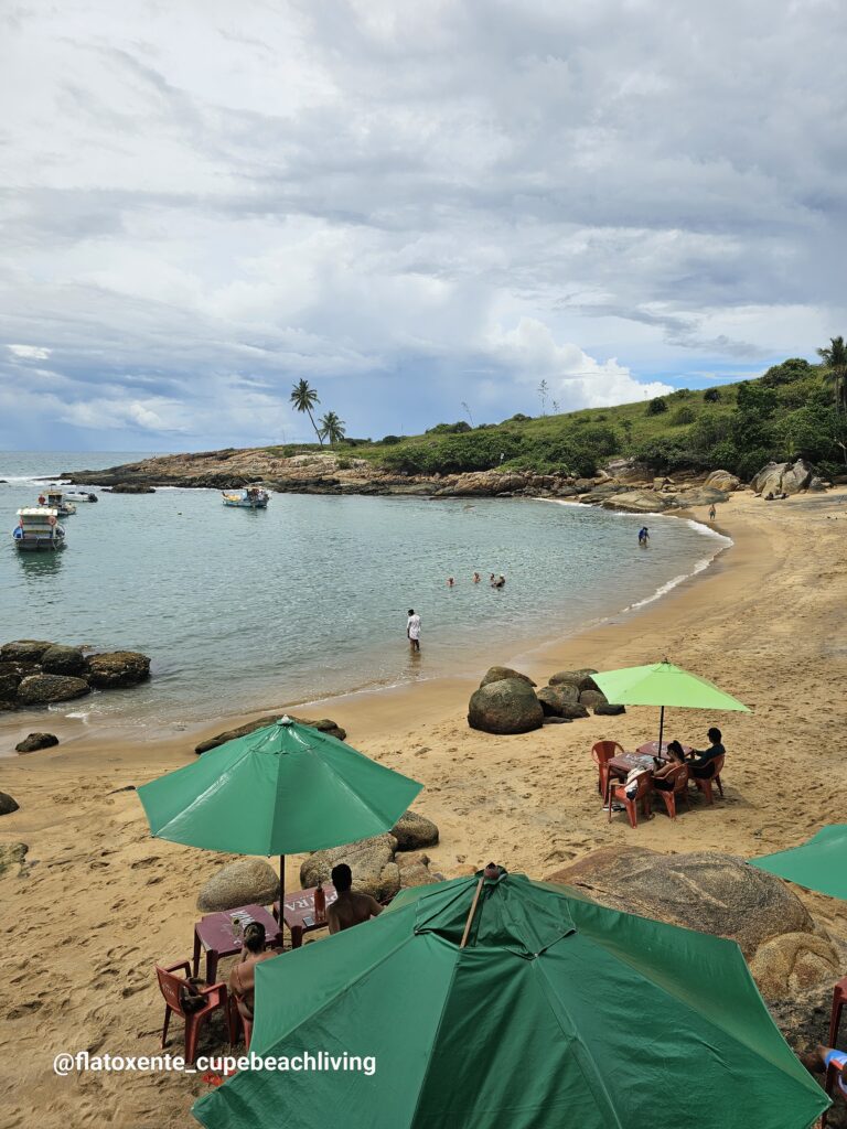 Strand von Calhetas mit grünen Sonnenschirmen, Felsen und Booten in ruhiger Bucht