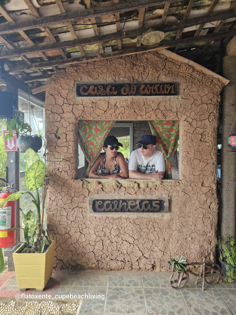 Paar lehnt sich aus dem Fenster eines rustikalen Lokals mit Lehmwand am Praia de Calhetas