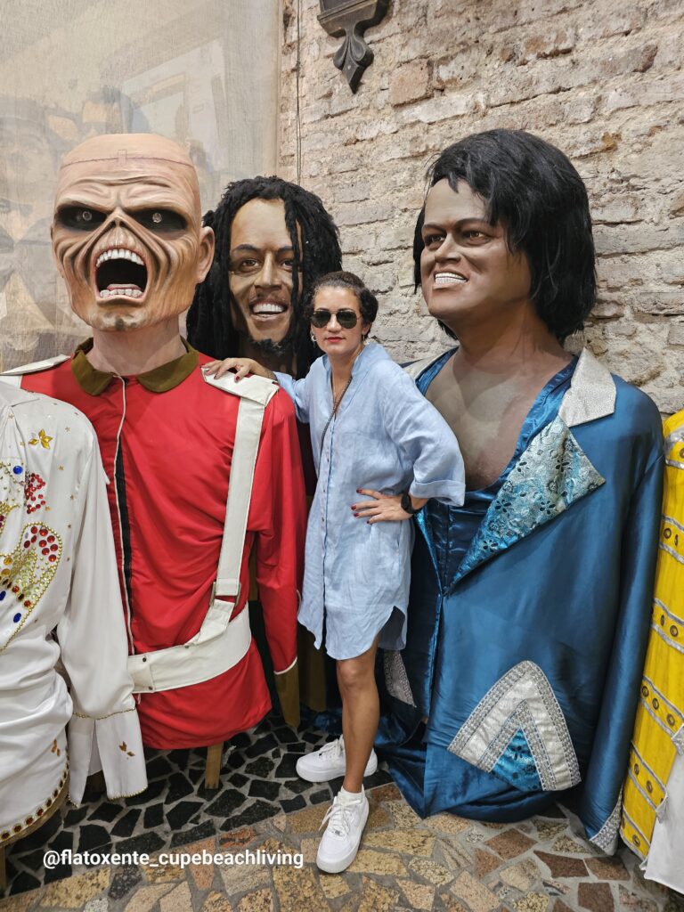 Frau posiert zwischen lebensgroßen Wachsfiguren internationaler Musikstars vor einer Backsteinwand