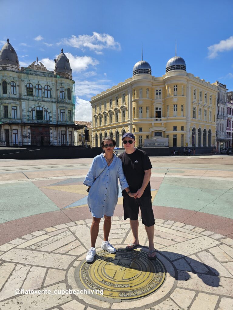 Paar steht auf dem kreisrunden Bodenmosaik des Praça Marco Zero in Recife, im Hintergrund historische Kolonialgebäude