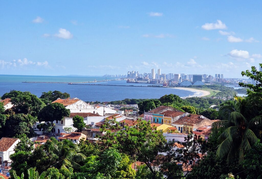 Panoramablick von Olinda auf die Bucht, den Strand und die Skyline von Recife bei Tageslicht, bunte Kolonialhäuser im Vordergrund