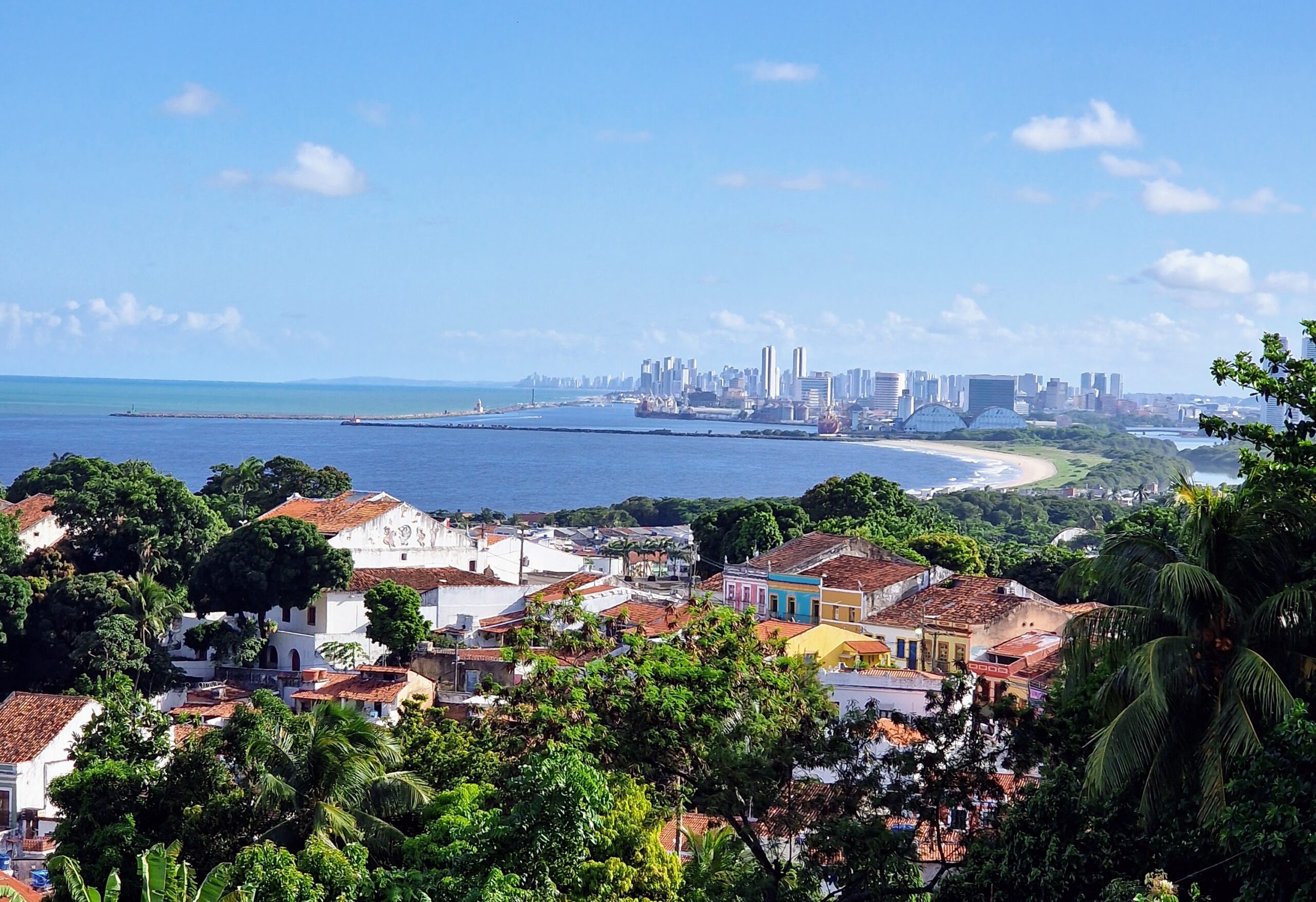 Panoramablick von Olinda auf die Bucht, den Strand und die Skyline von Recife bei Tageslicht, bunte Kolonialhäuser im Vordergrund