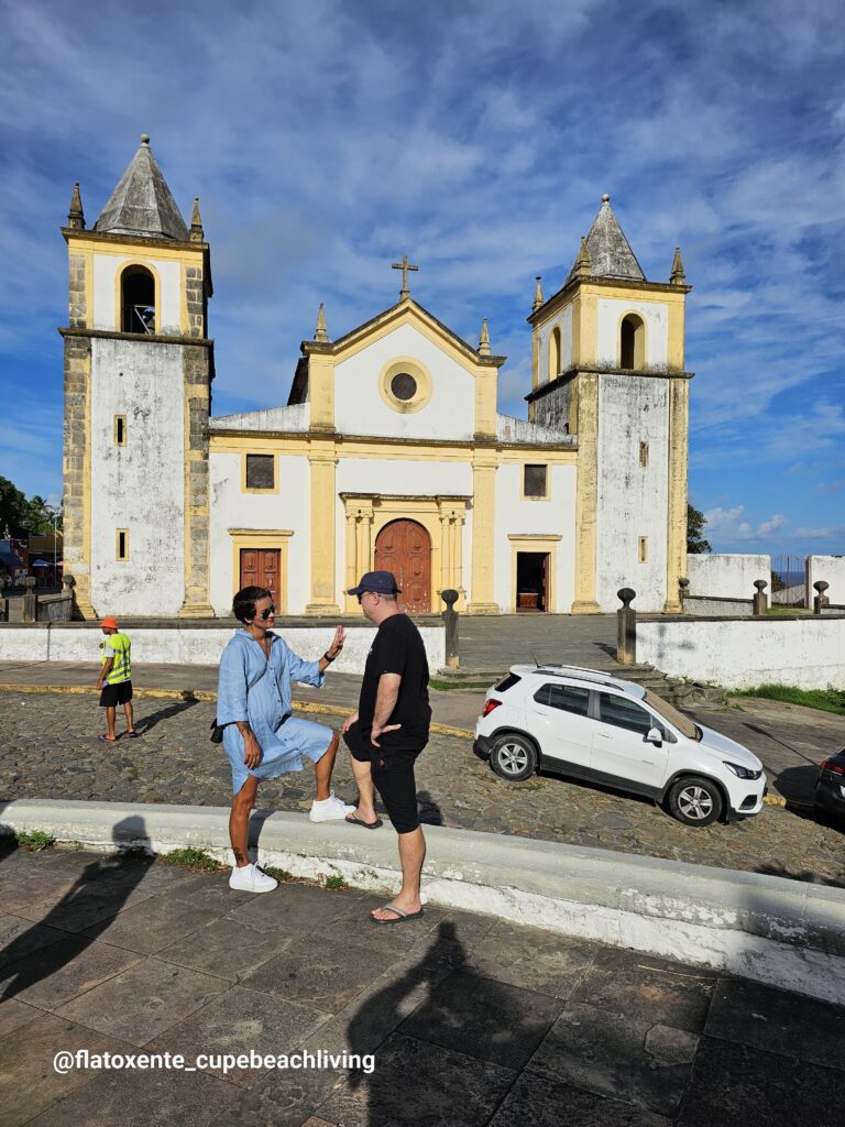 Paar steht auf einer Mauer vor der weiß-gelben Kolonialkirche Igreja da Sé in Olinda, Brasilien