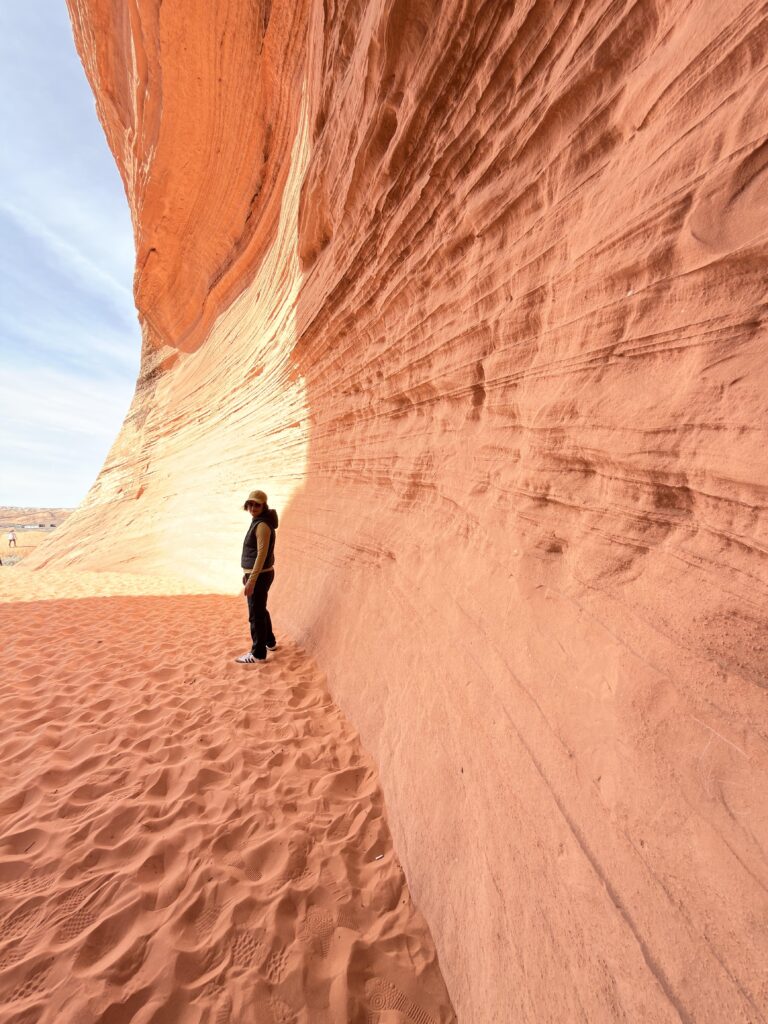 Person steht am Rand einer roten Sandsteinwand bei Bidii the Arch, Licht- und Schattenspiel auf dem Fels