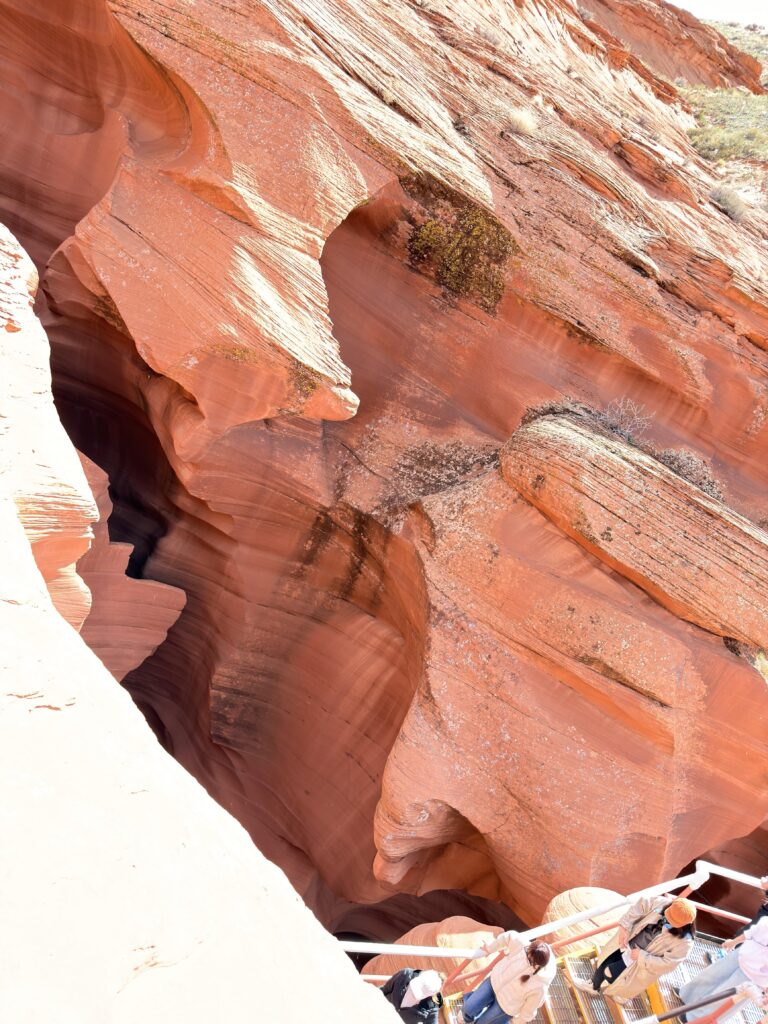 Detailaufnahme der geschichteten roten Sandsteinformationen im Lower Antelope Canyon mit Besuchern auf Treppen im unteren Bildbereich