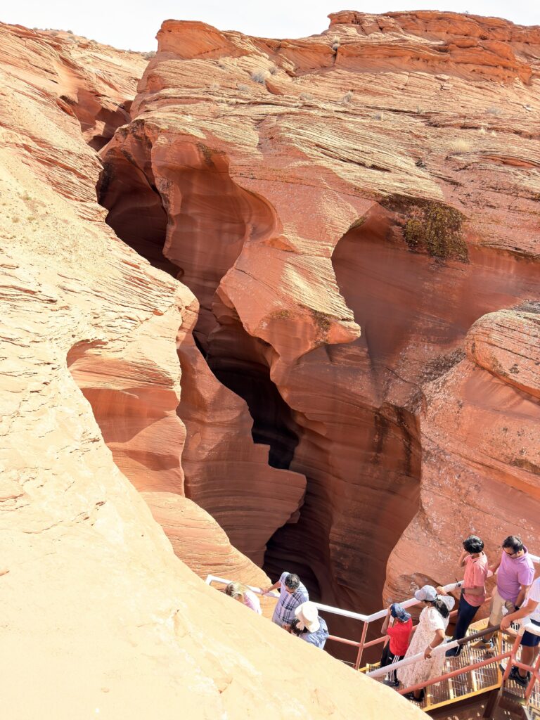 Touristen steigen über Metalltreppen in die enge rote Felsschlucht des Lower Antelope Canyon hinab