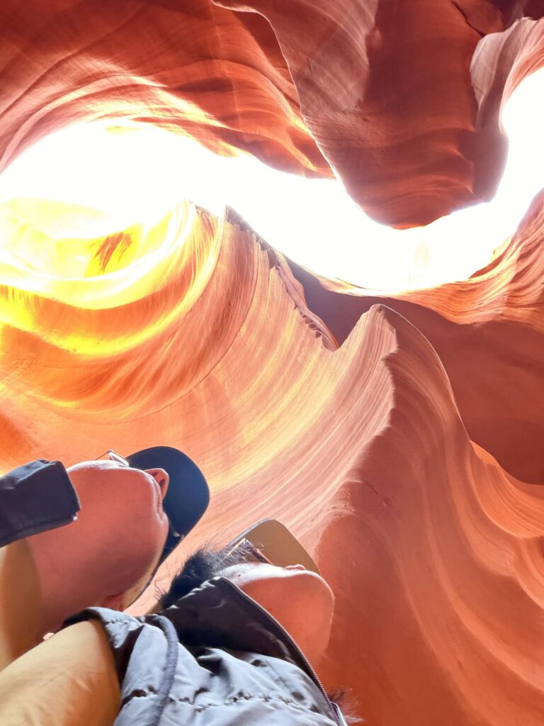 Selfie von unten aufgenommen im Lower Antelope Canyon mit hellem Lichteinfall und den geschwungenen Sandsteinwänden im Hintergrund