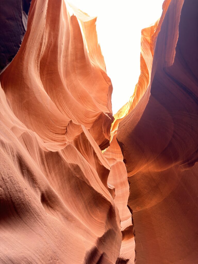 Blick von unten nach oben durch eine enge Felsspalte im Lower Antelope Canyon, Sonnenlicht bricht durch die Öffnung