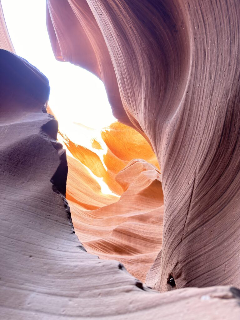 Wellenförmige orangefarbene Sandsteinwände im Lower Antelope Canyon mit hellem Lichteinfall im Hintergrund