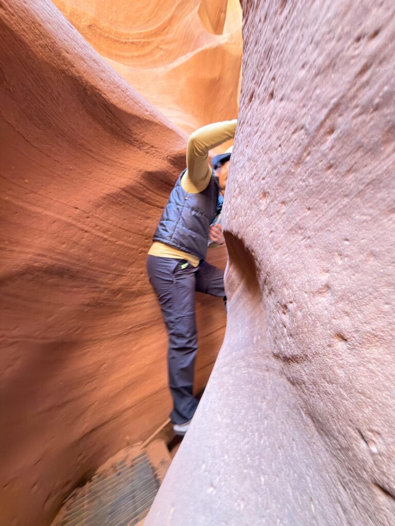 Person klettert durch eine enge Sandsteinpassage im Lower Antelope Canyon