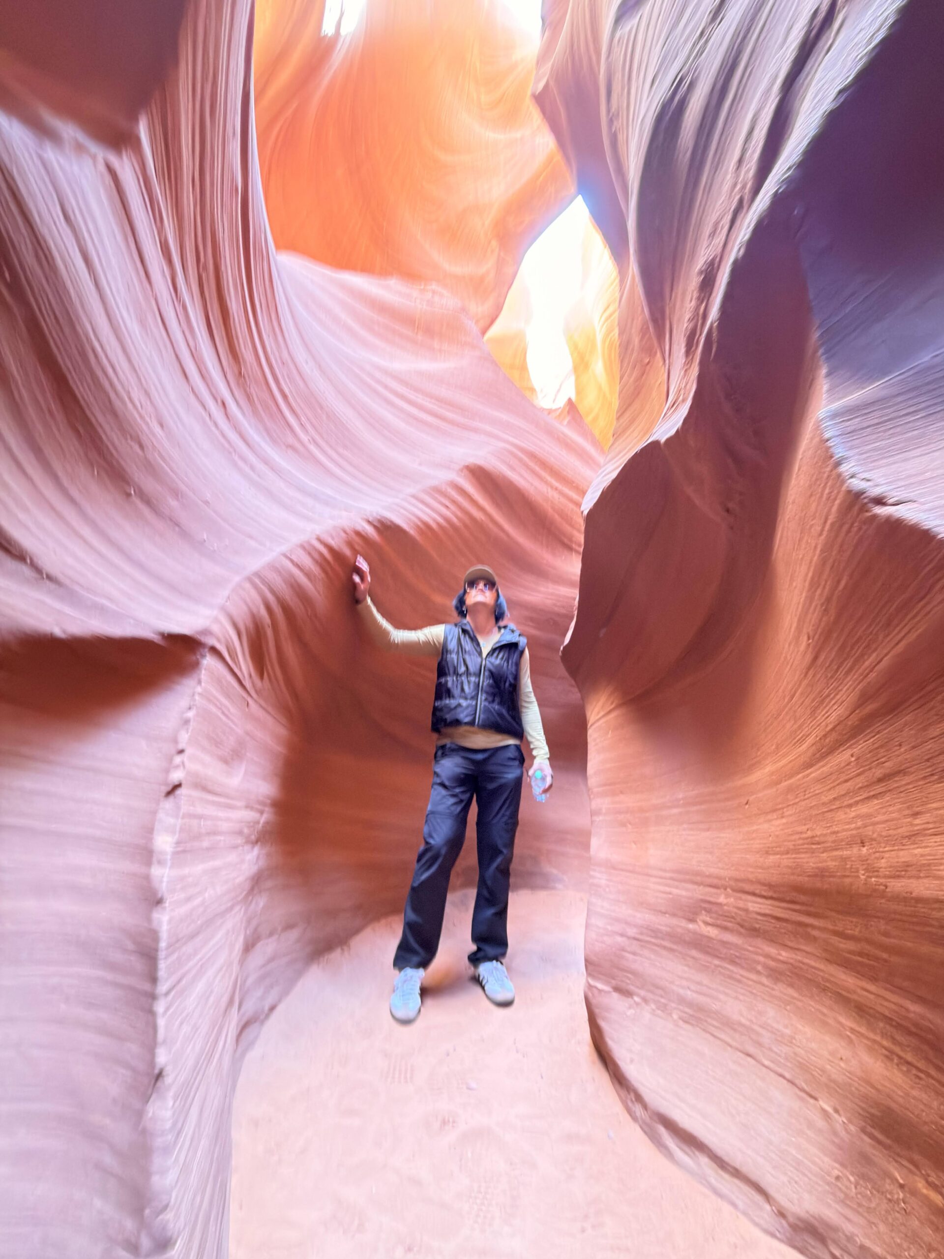 Person steht in der schmalen Sandsteinschlucht des Lower Antelope Canyon und blickt nach oben zum Lichtschlitz