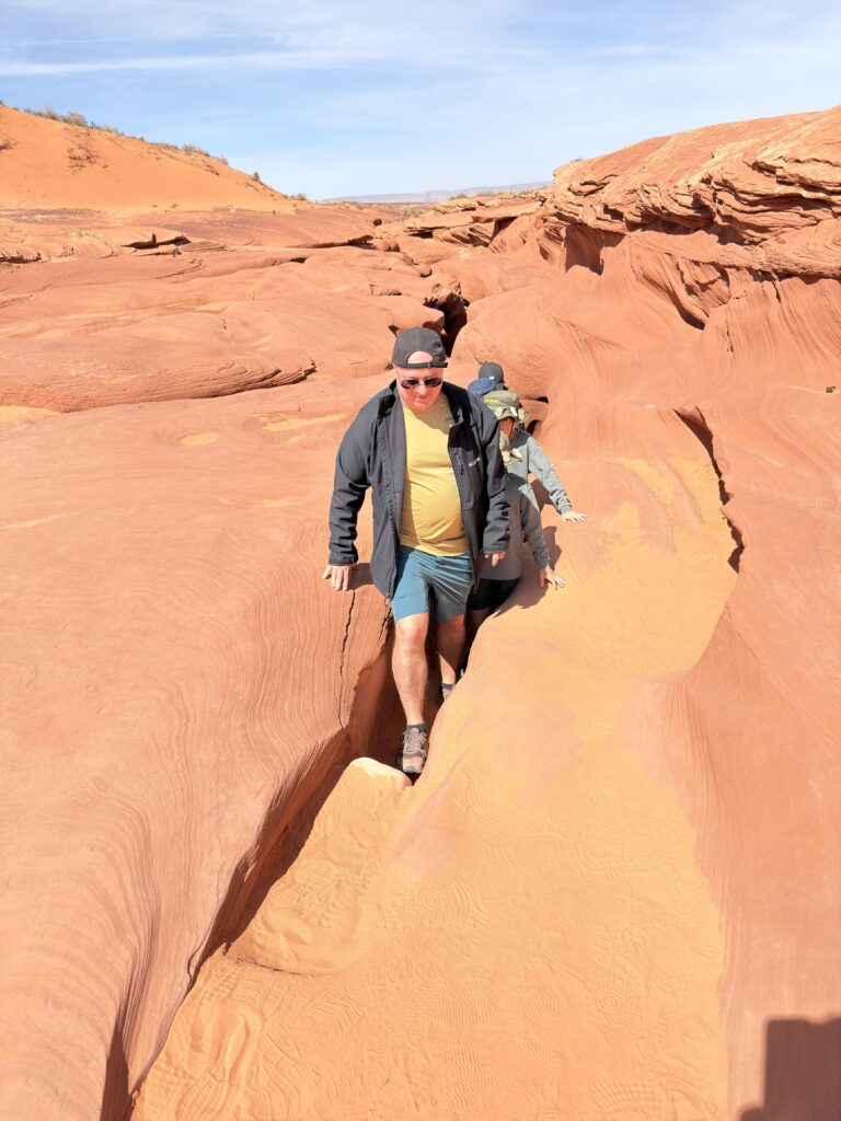Gruppe von Wanderern geht durch eine schmale Felsspalte in der roten Sandsteinoberfläche über dem Lower Antelope Canyon