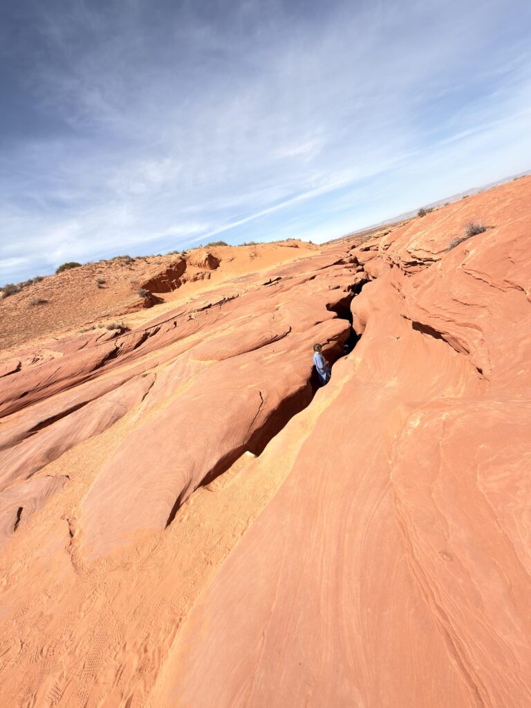 Person steht in einer schmalen Felsspalte in der roten Sandsteinoberfläche am Ausgang des Lower Antelope Canyon