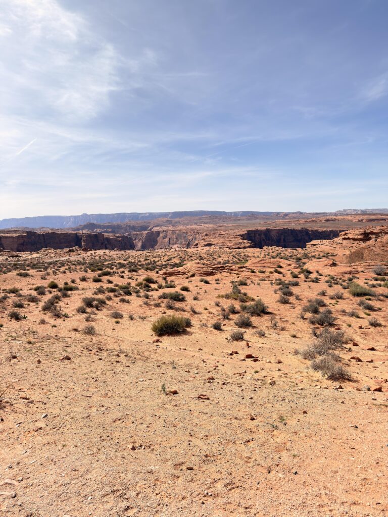 Weite Wüstenlandschaft mit Blick auf den Canyon und Besucher am Horseshoe Bend in der Ferne