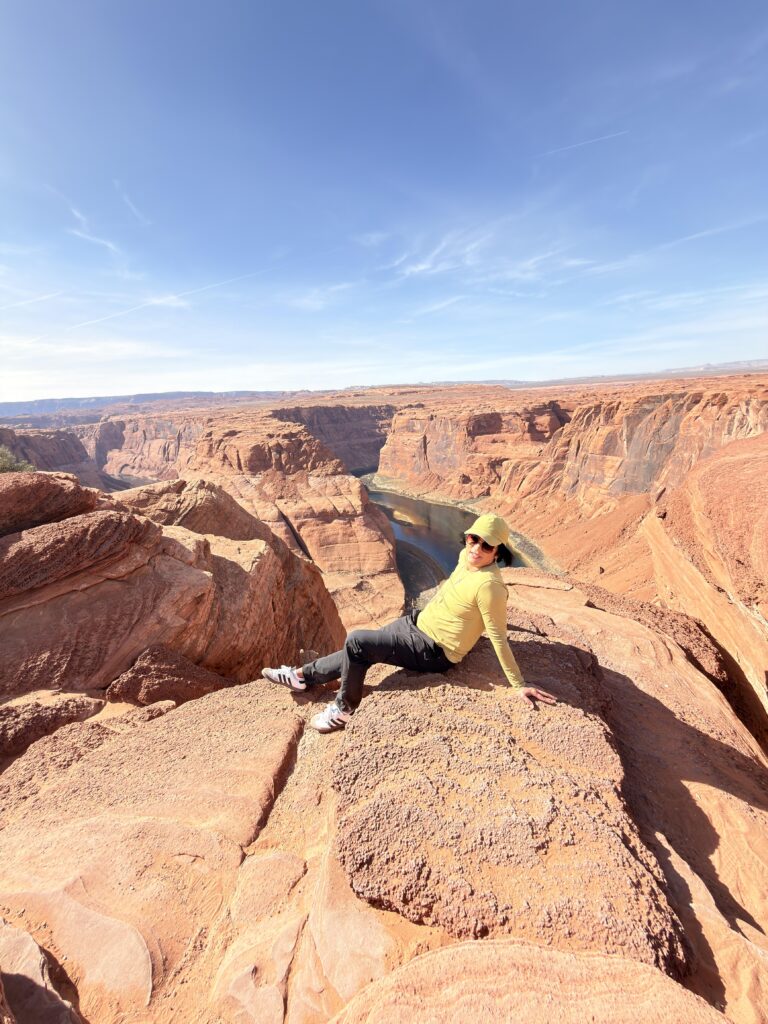 Person sitzt auf einem Felsvorsprung mit Blick auf die Flussschleife des Colorado River am Horseshoe Bend
