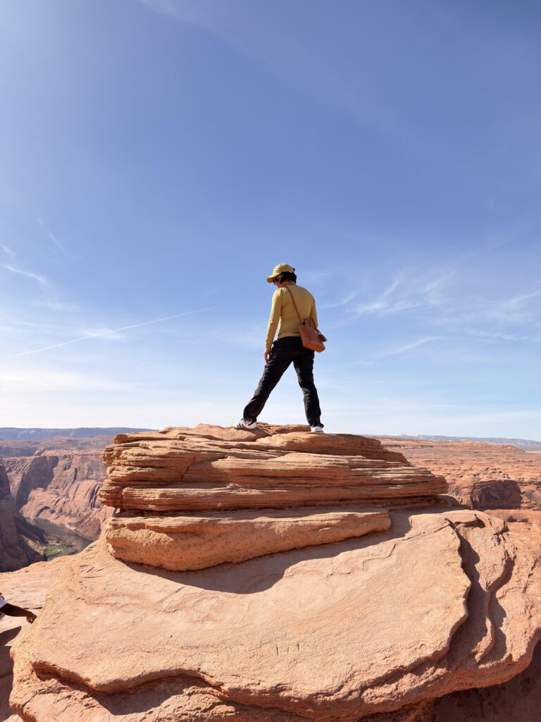 Person steht auf geschichteten Sandsteinfelsen mit Blick auf den Canyon am Horseshoe Bend