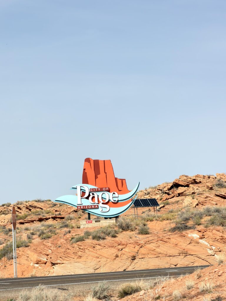 Stilisiertes Schild "City of Page Arizona" mit rotem Felsmotiv auf einem Hügel in der Wüstenlandschaft