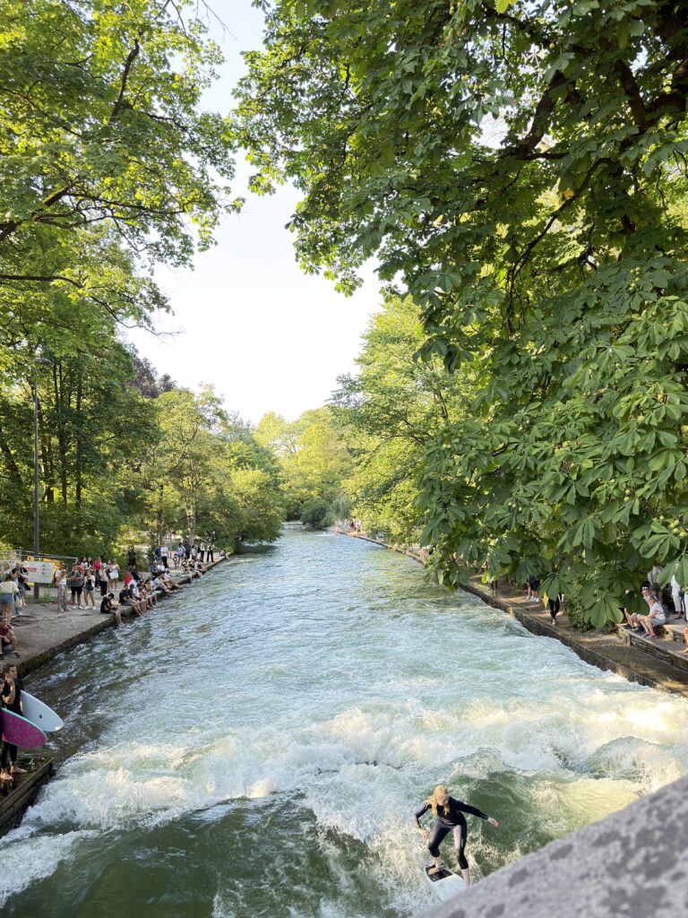 Surferin auf der Eisbachwelle zwischen grünen Bäumen im Englischen Garten
