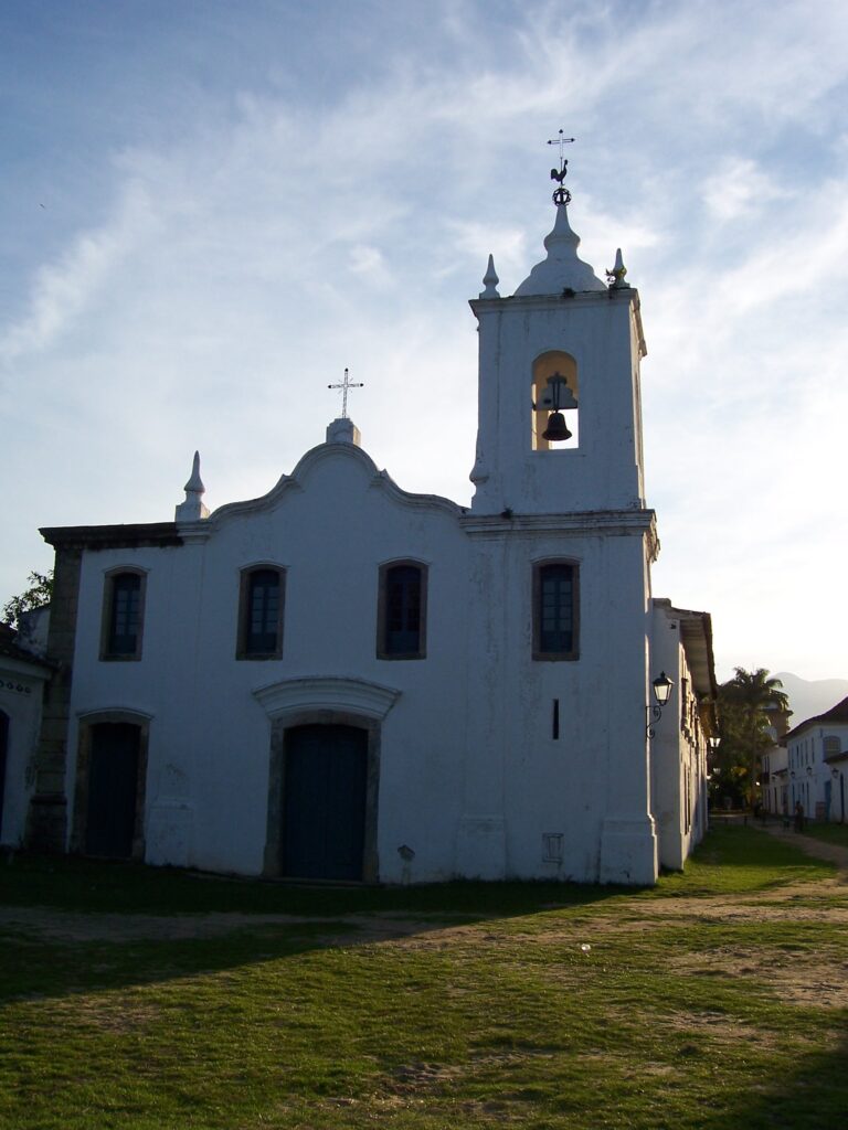 Weiße Kolonialkirche mit Glockenturm und Kreuz im Gegenlicht der Abendsonne, Paraty, Brasilien