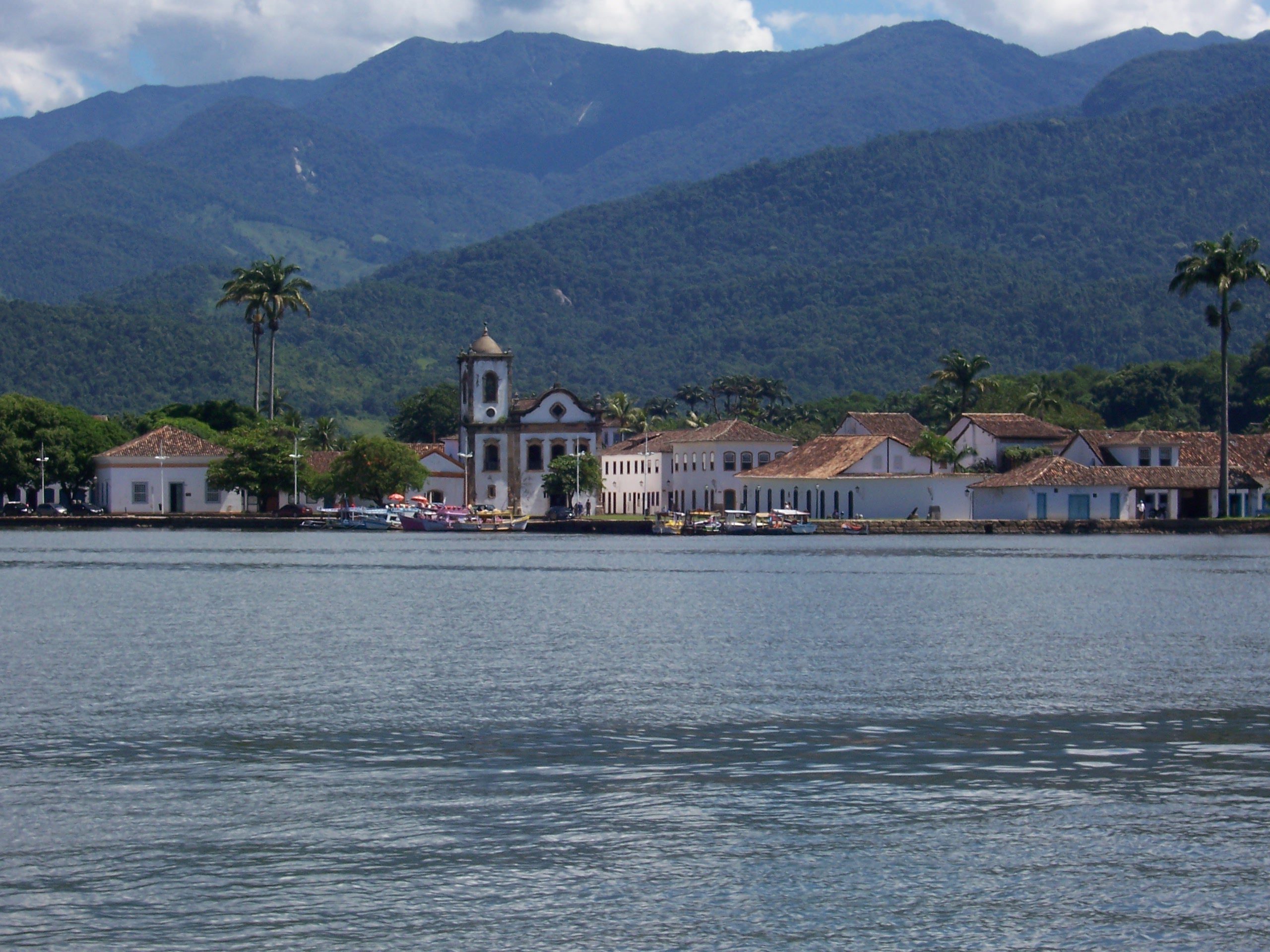 Blick vom Wasser auf die weiße Altstadt von Paraty mit Kirchturm vor bewaldeten Bergen, Brasilien